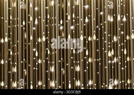 A close-up of a golden metallic surface featuring vertical lines and teardrop-shaped light reflections, creating a shimmering decorative pattern suita Stock Photo