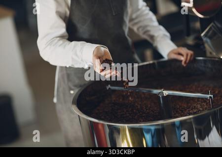Coffee cooling in roaster machine at coffee roasting process. Young woman barista drops coffee beans in hands Stock Photo
