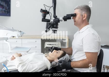 Male dentist using dental microscope treating patient teeth at dental clinic office. Medicine, dentistry and health care concept Stock Photo