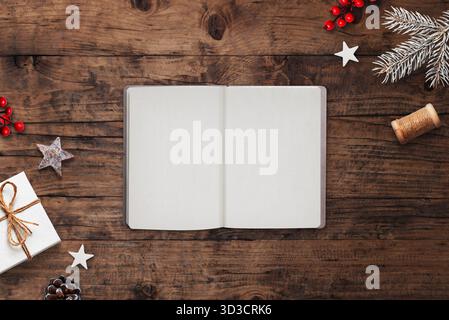 Top view of open notebook on rustic wooden table with Christmas decorations, pine branches, gift, and red berries, holiday greeting concept Stock Photo