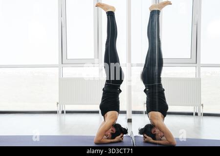 Young attractive yogi woman practicing yoga concept, standing in salamba sirsasana exercise, headstand pose, working out, wearing sportswear, full len Stock Photo