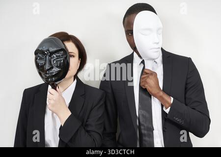 African man and Caucasian woman wearing black suits hiding face with masks Stock Photo