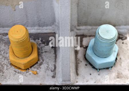 Two industrial bolts and nuts in blue and yellow on metal base plate. Stock Photo