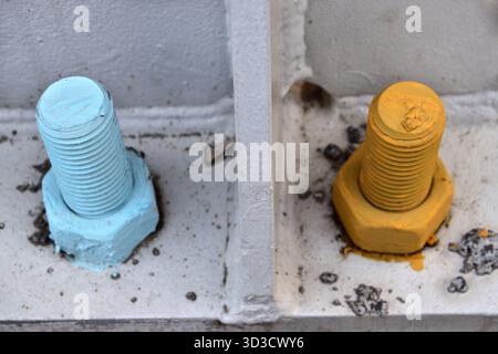 Two industrial bolts and nuts in blue and yellow on metal base plate. Stock Photo