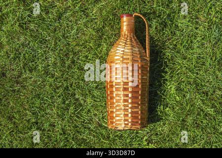 Rattan wine bottle laying on green grass lawn Stock Photo