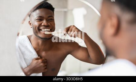 Cheerful African American Man Enjoys Morning Teeth Cleaning Routine in Modern Bathroom Stock Photo