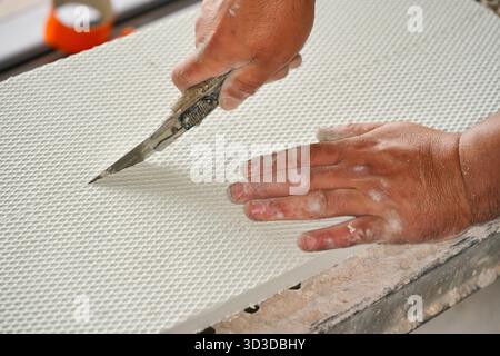 Man cutting polystyrene foam heat insulation with old retractable utility knife, closeup detail Stock Photo