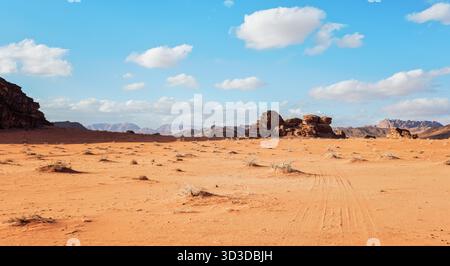 Orange red sand desert, rocky formations and mountains background, blue sky above - typical scenery in Wadi Rum, Jordan Stock Photo