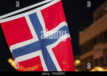 Norwegian flag hanging from a pole in Tromso city centre in Christmas period after dusk, Norway Stock Photo