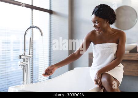 Young Black Woman Enjoys a Relaxing Moment Preparing for a Bath in a Stylish Bathroom Stock Photo
