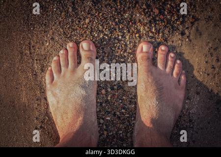 Close up of a feet of a man standing on the beach in summer Stock Photo
