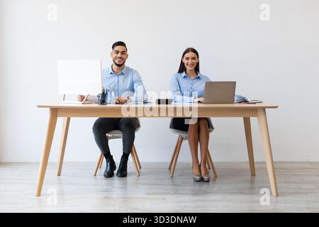 Colleagues Enjoying Teamwork at Office Desk While Using Laptops and Smiling for Camera Stock Photo