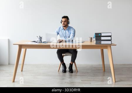 Focused Arab Man Works on Laptop at Desk in Modern Office Setting During Daytime Stock Photo