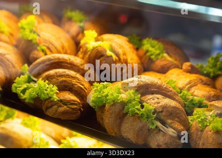 Tasty and fresh croissant sandwiches with ham and salad in a display case. Deli counter cooler with take out food Stock Photo