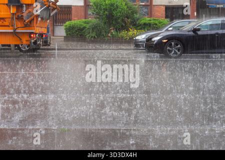 Heavy downpour splashing across a city street, intense rain striking pavement and cars during an urban storm in Hungary. Stock Photo