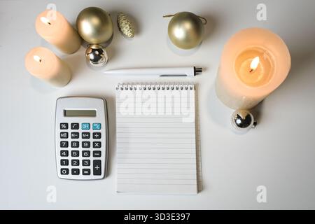 Blank notepad, calculator, candles and golden Christmas decoration, on a white table, mock-up, concept for holiday planning and finances, copy space, Stock Photo