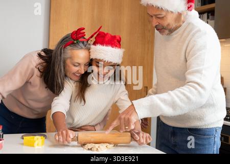 Diverse family baking cookies on home kitchen counter rolling dough with wooden pin and star cutter Stock Photo