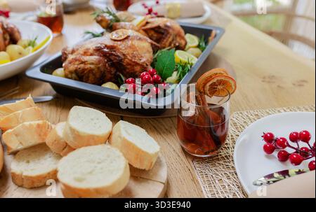 Two roast chickens resting in black pan on wooden table, with sliced bread and spiced beverage Stock Photo