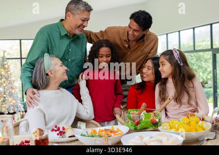 Multi-generation family gathering at table sharing bowls of salad with Christmas tree backdrop Stock Photo