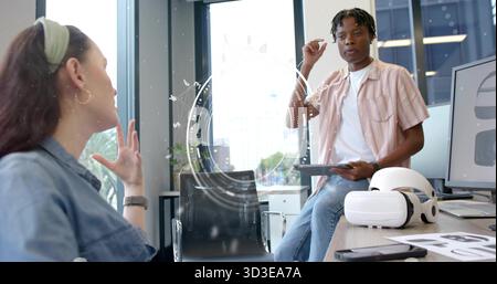 Presenting Black man gesturing with tablet near VR headset, sketches, monitor in office, copy space Stock Photo