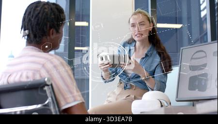 Female engineer explaining holographic interface in office, with smartphone, VR headset and monitor Stock Photo