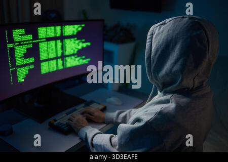 Hacker using the computer. Man in a hoodie breaks the access to steal information and infects computers and systems Stock Photo