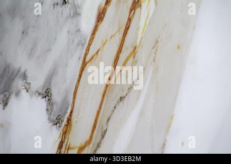 Detailed close-up of marble veins forming organic golden and gray lines on a white surface. Stock Photo