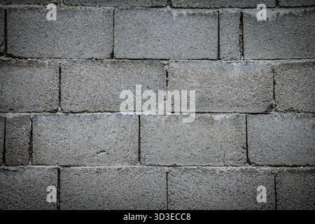 Closeup of a concrete masonry unit wall with gray, rough texture. Staggered bond and mortar joints create a repeating pattern, offering an industrial Stock Photo