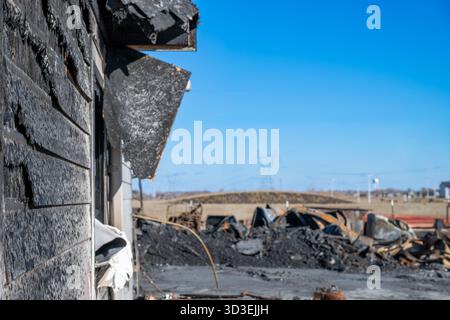 Burnt remains of a building in a rural landscape after a fire on a clear day with power lines in the background Stock Photo