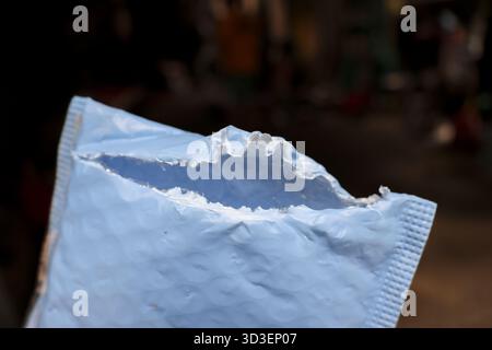 Close up of torn open blue package or sachet with jagged edge. empty bag reveals its inside texture against dark background, showing sense of consumpt Stock Photo