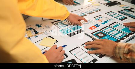 A vibrant workspace bustling with designers collaborating on a mobile app prototype, showcasing user interface wireframes, tools, and creative Stock Photo