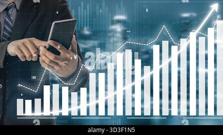A business professional studies financial data trends using a smartphone while surrounded by visuals of upward graphs and modern analytics. The image Stock Photo