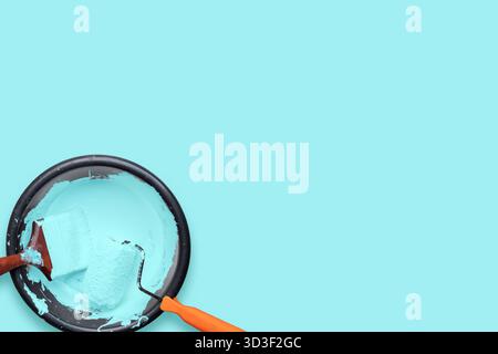 Flat lay composition showing paint roller and brush dipped in pastel blue paint on a tray with matching background, symbolizing creativity, renovation Stock Photo