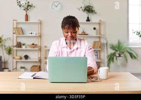 Young smiling African American woman sitting at desk, using laptop, studying or working online. Stock Photo