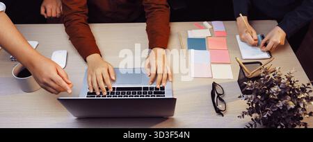 A dynamic workspace featuring a laptop and vibrant sticky notes, highlighting hands of individuals collaborating in a creative brainstorming session Stock Photo