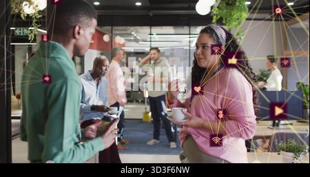Woman wearing pink cardigan holding coffee cup and saucer in office lounge with plants, copy space Stock Photo