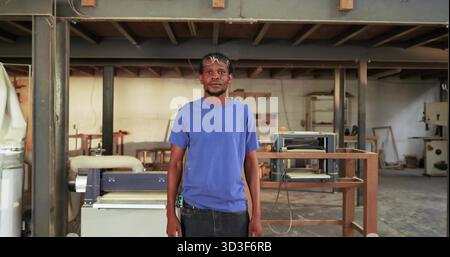Standing carpenter wearing safety glasses holding tape measure in woodworking workshop with planer Stock Photo
