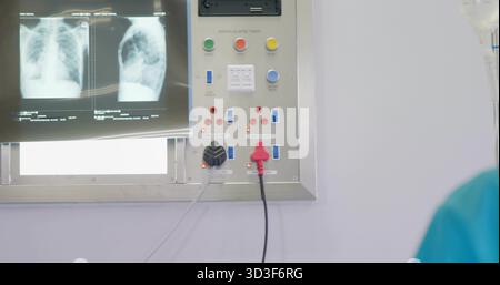 Showing chest X-rays on light box, control panel, iv-drip bag, teal scrubs in hospital, copy space Stock Photo