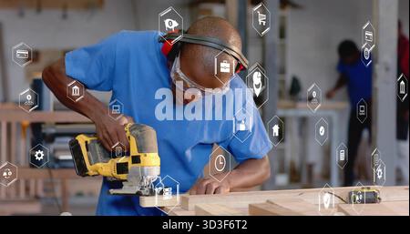 Carpenter wearing goggles cutting wooden plank in workshop, with yellow jigsaw and digital icons Stock Photo