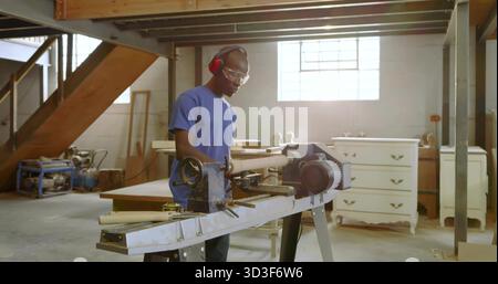 Mid adult male carpenter shaping spindle on lathe in woodshop, with goggles and earmuffs Stock Photo