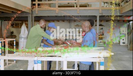 Gathering at sawhorses, four men collaborating in workshop with planks and red power tool Stock Photo