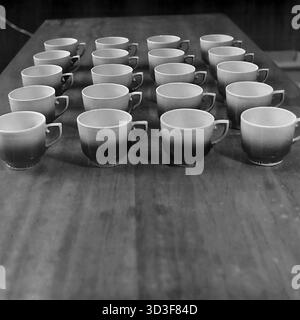 An archival photo from the 1990s shows consumer goods (TNP) from the AIZ (Armature-Insulator Plant) in Sloviansk, Ukraine. This is a display of finished products. Twenty identical ceramic cups are arranged in four neat rows of five on a wooden table. The cups feature a distinctive faceted design and a two-tone gradient glaze. This image shows the consumer goods production line of a major industrial factory. This captures industrial history in the peaceful Donbas before the war. Stock Photo