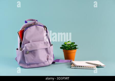 A backpack filled with stationery with flowers on an isolated blue background with a place for text, the September 1 concept for schoolchildren and st Stock Photo