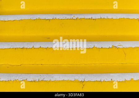 Worn concrete steps, painted bright yellow, revealing peeling white edges as an abstract pattern Stock Photo