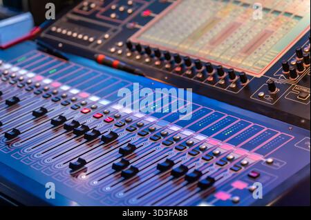 Close up of a mixing console with illuminated buttons and faders, creating a vibrant atmosphere in a music production setting Stock Photo