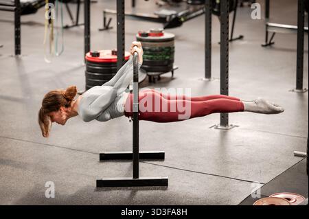 Woman holding calisthenics horizontal back lever exercise, demonstrating strength and fitness in a gym Stock Photo