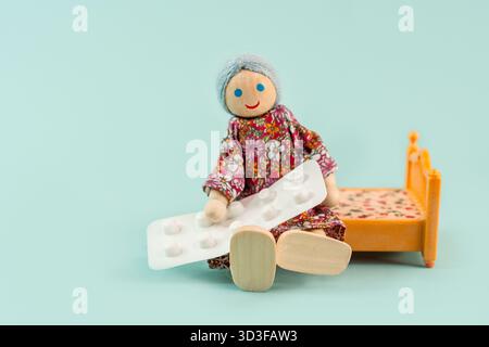 Toy pensioner elderly granny woman sits on the bed and holds a blister of pills, elderly healthcare Stock Photo