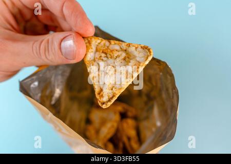 Men's hands eat corn chips nachos from a package on blue table background. Close up, point of view shot. Stock Photo
