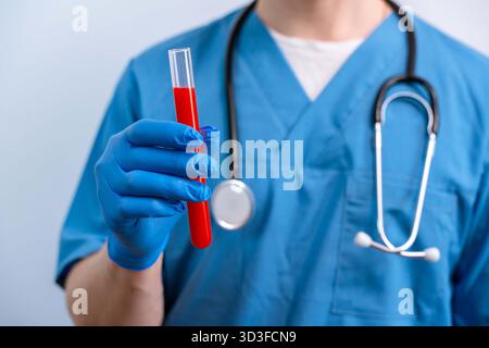 Young man Caucasian doctor in a blue uniform holds a flask with a blood test on an isolated background. Stock Photo