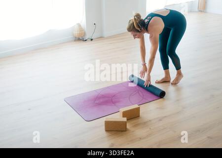 Woman rolling up purple yoga mat after session. Stock Photo